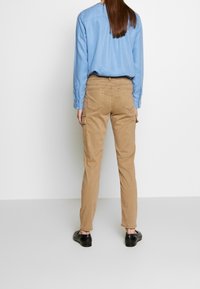 Spodnie bojówki koloru khaki z bocznymi kieszeniami i przeszyciami, w połączeniu z jasnoniebieską, długorękawową koszulą, widziane od tyłu.