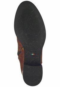 Semelle en cuir marron avec un dessous en caoutchouc noir texturé, comportant un logo et le texte "Fabriqué en Italie" près d'un petit détail du drapeau italien.