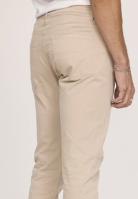 Pantalons en coton beige avec une coupe droite, poches arrière visibles et détails de couture subtils. Texture lisse, design mi-mollet.
