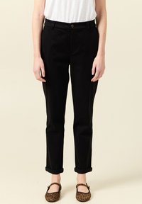 Czarne bawełniane spodnie o prostym kroju z podwiniętymi mankietami, z zapięciem na guziki z przodu i kieszeniami bocznymi. Noszone z butami w panterkę.