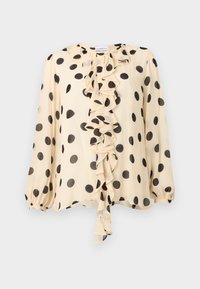 Κρέμ μακρυμάνικο μπλούζα με μεγάλα μαύρα πουά και ένα κεντρικό καταρράκτη βολάν στο μπροστινό μέρος.