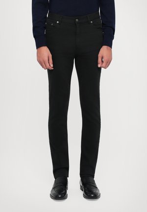 Sorte denimbukser med slim fit, fem lommer, metalhardware og kontrastsytråd. Båret med sorte dressko.
