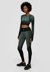 Sportliches Set mit langärmligem Oberteil und hochgeschnittenen Leggings. Hergestellt aus atmungsaktivem, strukturiertem Stoff in Dunkelgrün und Schwarz.