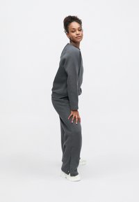 Sweatshirt e calças de treino cinzentas em mistura de algodão com corte descontraído. Destacados por aberturas laterais, combinados com ténis desportivos brancos.