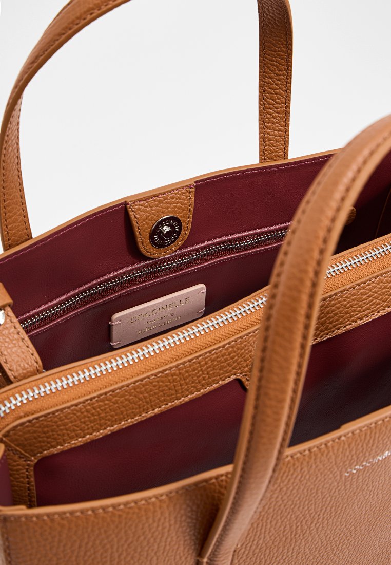 Hellbraune Ledertasche mit strukturiertem Äußeren, burgunderroter Innenauskleidung, einem zentralen Reißverschlussfach und doppelten Schulterriemen.