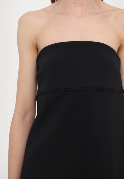 Svart stroppeløs kjole med en glatt, matt tekstur. Har et tettsittende liv og en horisontal søm i midjen. Enkel, minimalistisk design.
