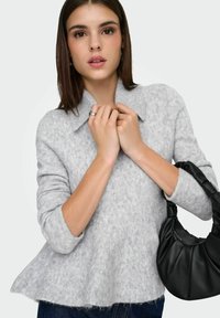 Světlě šedý pletený svetr s límcem a lampionovými rukávy, doplněný černou kabelkou s nařaseným designem.