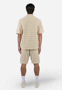 Ensemble en tricot beige comprenant un polo et un short, avec des rayures horizontales et diagonales, des manches courtes, une coupe décontractée et des ourlets roulés.