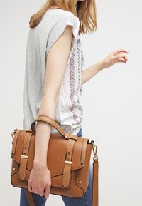 Bruine leren handtas met een gestructureerd ontwerp, voorzien van een voorflap, goudkleurige hardware en een afneembare schouderband.