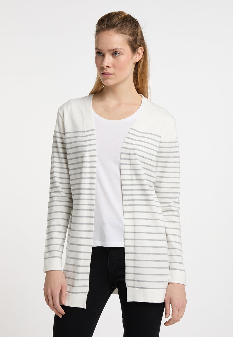 Cardigan bianco con strisce grigie, davanti aperto, maniche lunghe e una texture morbida, indossato sopra una maglietta bianca e jeans neri.