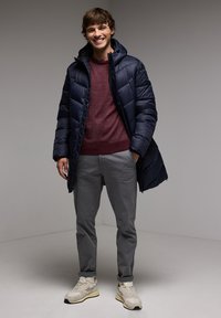 Námorní pufovací kabát s kapucí, vínový svetr, šedé chinos a béžové tenisky. Hladká textura, prošívaný design a funkční zipy.