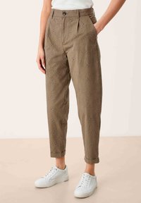 Khaki broek met uitsparingen, met een ontspannen pasvorm en opgerolde manchetten. Gecombineerd met witte sneakers, wat een casual uitstraling geeft.