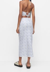 Tenue deux pièces composée d'un haut dos nu style dos-nu à col halter blanc à imprimé floral bleu et d'une jupe assortie mi-longue. Tissu texturé, détail simple avec un nœud.
