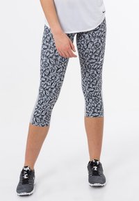 Šedé legíny capri se vzorem vyrobené z elastického materiálu, zdobené geometrickým designem, v kombinaci s černými sportovními botami.