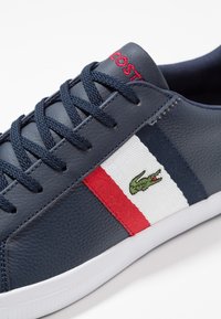 Leather sneaker in navy blue with textured upper, white rubber sole, red and white striped accents, and green embroidered crocodile logo.