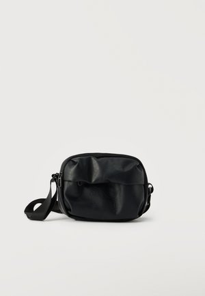 Sac bandoulière Puma noir avec sangle réglable, poche avant zippée et logo Puma embossé discret sur matériau lisse.
