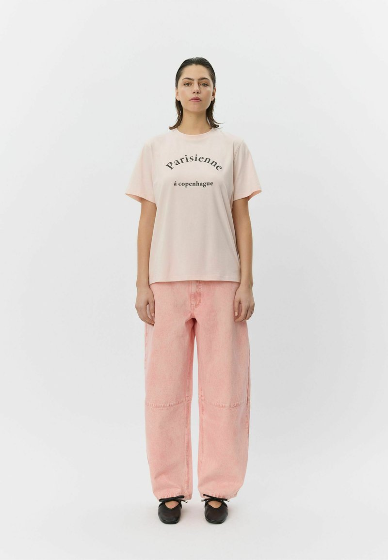 Tricou roz deschis cu text negru care spune "Parisienne à Copenhague", asortat cu pantaloni largi din denim roz deschis și balerini negri.