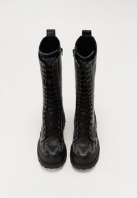 Czarne skórzane buty wojskowe z białymi dekoracyjnymi przeszyciami, wysokim fasonie, sznurowane z przodu oraz z bocznymi zamkami dla łatwego zakładania.