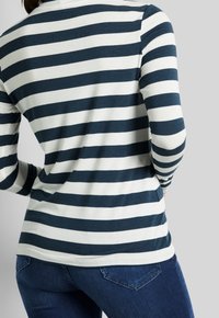Chemise à rayures bleu marine et blanche à manches longues avec un ourlet arrondi, fabriquée en tissu doux, associée à un jean ajusté bleu foncé.