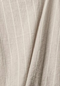 Tissu beige clair avec des rayures blanches verticales, présentant un tissage texturé qui ajoute de la profondeur et de la dimension à la surface.