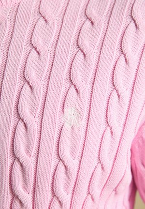 Artimas šviesiai rožinės pynimo megztos medžiagos vaizdas, kuriame matomas išsamus susuktos virvės raštas ir subtilus baltos spalvos išsiuvinėtas logotipas.