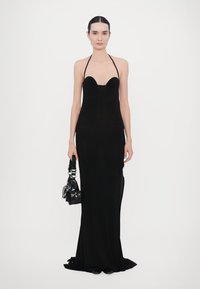 Black, form-fitting, sleeveless dress with a sweetheart neckline. Model holding a small, structured black handbag. Simple and elegant design.