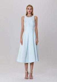 Robe sans manches bleu clair avec un corsage ajusté, une jupe plissée et un décolleté orné. Complétée par des talons blancs à brides.