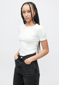 Λευκό εφαρμοστό μπλουζάκι με κοντά μανίκια, ριμπ υφή, στρογγυλή λαιμόκοψη, συνδυασμένο με ψηλόμεσα μαύρα τζιν τζιν με μπροστινές τσέπες.