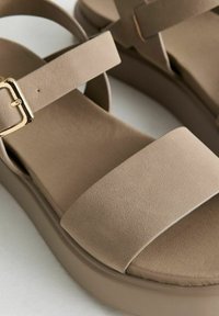 Sandali platform beige con cinturini larghi e morbidi e dettagli in oro. Parte superiore testurizzata con una soletta liscia e suola leggera.