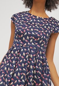 Granatowa sukienka z krótkimi rękawami, z wzorem kolorowych ptaków. Materiał wydaje się gładki i lekki, z dopasowanym gorsetem i rozkloszowaną spódnicą.