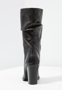 Bota de cuero negro hasta la rodilla con un diseño arrugado, punta redondeada y tacón cilíndrico alto, con una textura suave y detalles de costura.