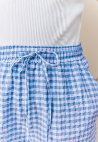 Pantalon à cordon de serrage vichy bleu et blanc avec taille élastique porté avec un haut sans manches blanc côtelé.