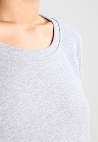 Grå kortärmad sweatshirt med rund halsringning, tillverkad av mjukt, texturerat tyg. Sömdetaljer är subtilt synliga längs axlarna.