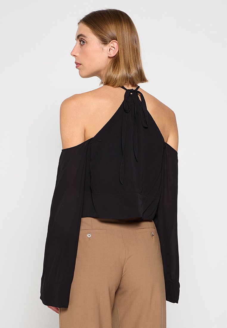 Top nero con scollo a halter e maniche scoperte, dettaglio nodoso sulla schiena e vestibilità corta, realizzato in tessuto morbido.