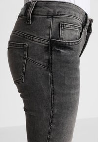 Jeans skinny de denim gris con una cintura alta, cinco bolsillos y costuras decorativas a lo largo del lateral, con una textura suave.