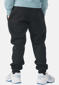 Zwarte trainingsbroek van zacht stof, taps toelopend bij de enkels; gedragen met witte sneakers met blauwe accenten.