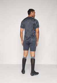 Maglia sportiva grigio scuro a maniche corte con un motivo geometrico, abbinata a pantaloni corti grigio scuro, calze nere fino al ginocchio e scarpini.