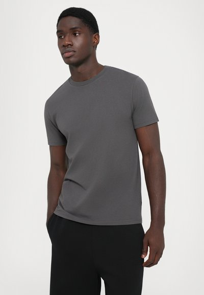 Grijze kortekoor t-shirt van zachte stof, met een klassieke ronde halslijn en een getailleerde pasvorm, gecombineerd met zwarte broek.