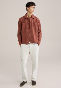 Roestkleurig linnen shirt met een casual pasvorm, knoopsluiting aan de voorkant, twee borstzakken en lange mouwen, gecombineerd met witte broeken en donkere espadrilles.