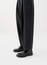 Czarne skórzane eleganckie buty sznurowane z perforowanymi zdobieniami, zaokrąglonym noskiem i niską, piętrową podeszwą, zestawione z luźnymi czarnymi spodniami.