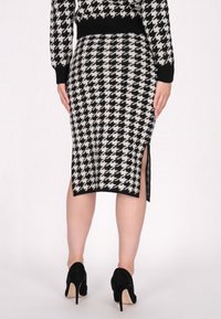 Tricot pencil skirt met een zwart-wit houndstooth patroon, gesplitst aan de zoom, gecombineerd met zwarte hoge hakken.