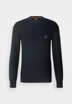 Gestreifter marineblauer Pullover mit langen Ärmeln, rundem Ausschnitt, strukturiertem Stoff und einem kleinen Logo-Patch auf der Brust.
