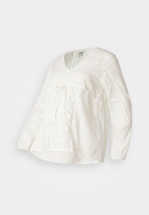 Biała bluzka z długim rękawem, wykończona w dekolt w kształcie litery V, z teksturowanej tkaniny i elastycznymi mankietami. Posiada związanie w pasie oraz koronkowe akcenty po bokach.