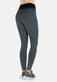 Schwarz- und grau-melierte, hochgeschnittene Leggings mit glatter Textur, figurbetontem Design und dezentem Muster. Tragen mit grauen Sportschuhen.