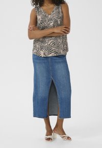 Mønstret ærmeløs top i beige og sort med V-udskæring, parret med en mid-længde blå denimnederdel med en frontslids. Hvide strophæle.