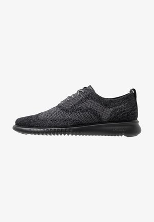 Zwarte gebreide sneakers met een laag profiel, textuur bovenkant, ronde neus en flexibele rubberen zool. Voorzien van grijze veters en een hieltab.