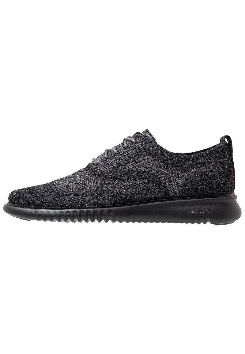 Sneakers in maglia nera con un design a profilo basso, tomaia testurizzata, punta rotonda e suola in gomma flessibile. Presentano lacci grigi e un linguetta sul tallone.