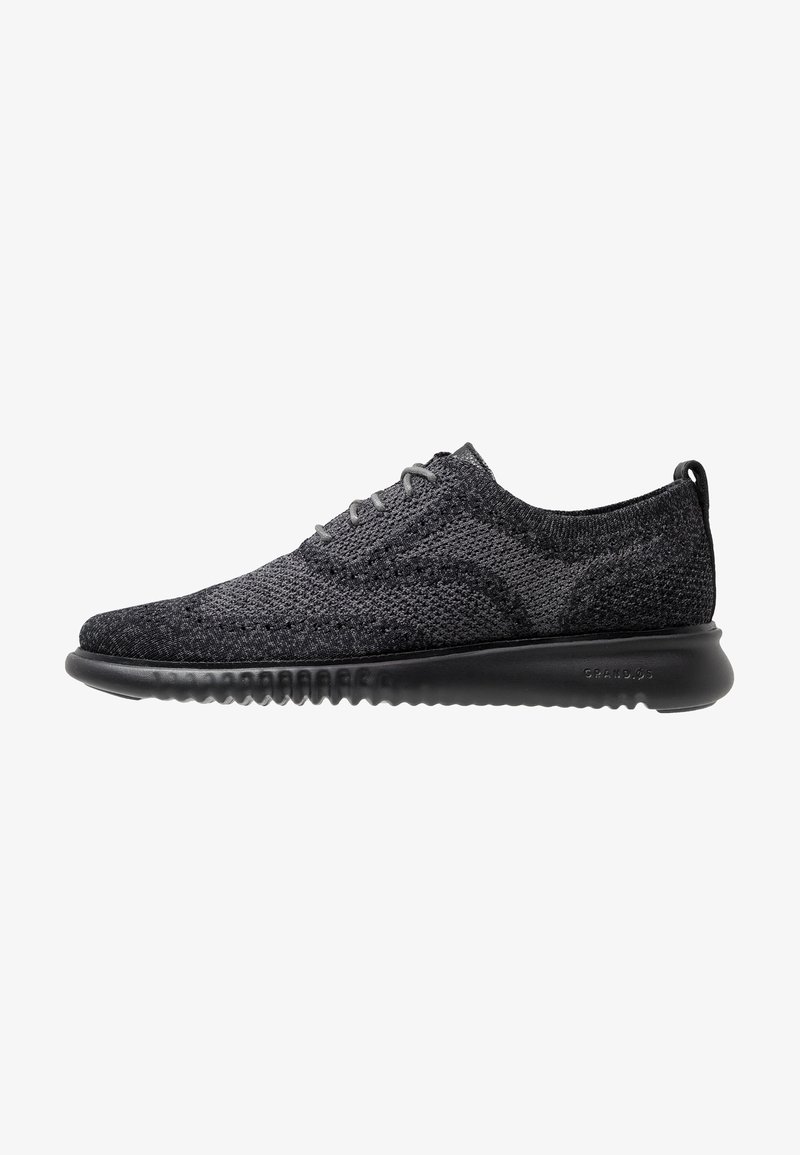 Sneakers in maglia nera con un design a profilo basso, tomaia testurizzata, punta rotonda e suola in gomma flessibile. Presentano lacci grigi e un linguetta sul tallone.