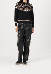 Pull noir en maille avec un empiècement à motifs en marron, blanc et beige, associé à un pantalon noir en similicuir taille haute avec des bandes latérales.