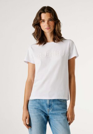 White cotton t-shirt featuring a "LONDON" graphic in rhinestones, with short sleeves and a relaxed fit. Worn with light blue jeans.